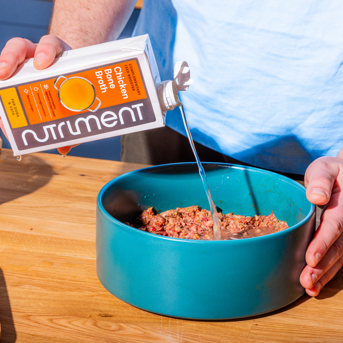 Pouring Chicken Bone Broth 500ml into ground meat in a blue bowl, supporting healthy digestion.