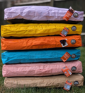 Stack of colorful dog beds with tags on a grassy background