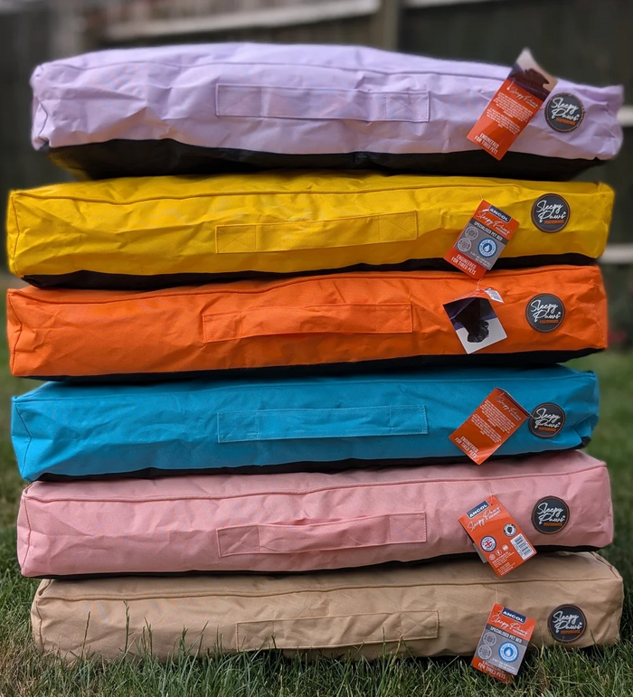 Stack of colorful dog beds with tags on a grassy background